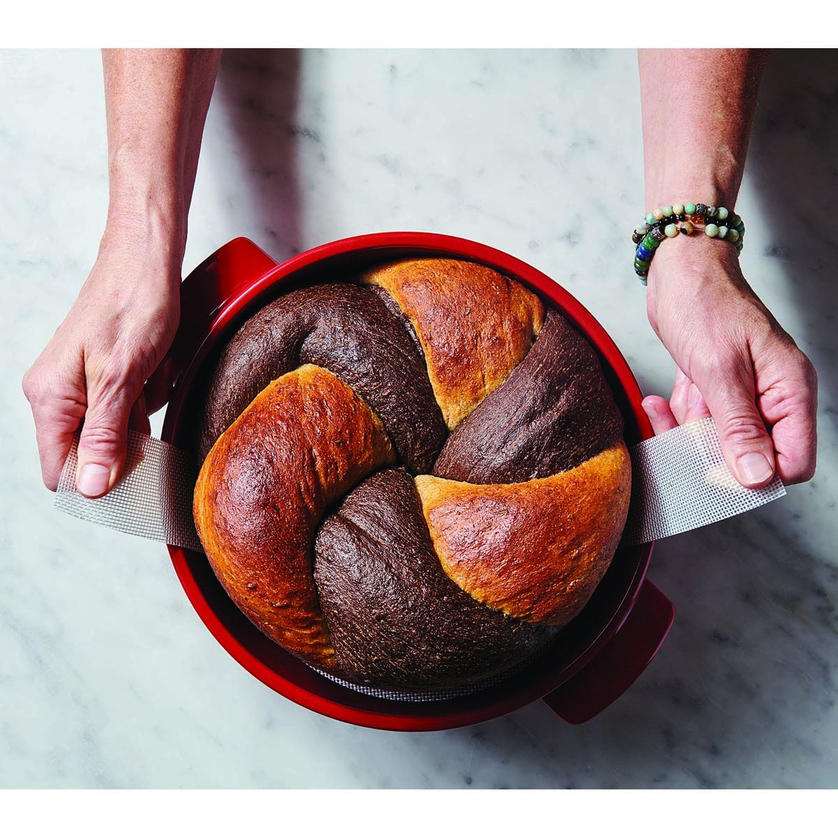 Bread in a red bundt cake pan held by two hands on a marble surface