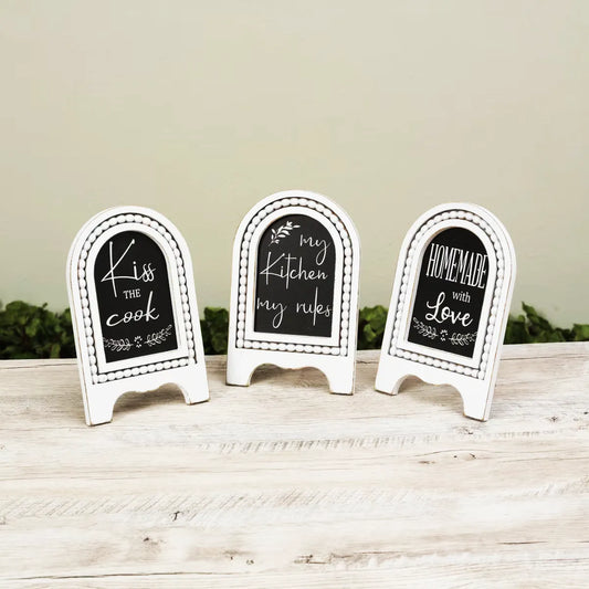 Three decorative chalkboard signs on a wooden surface with a neutral background