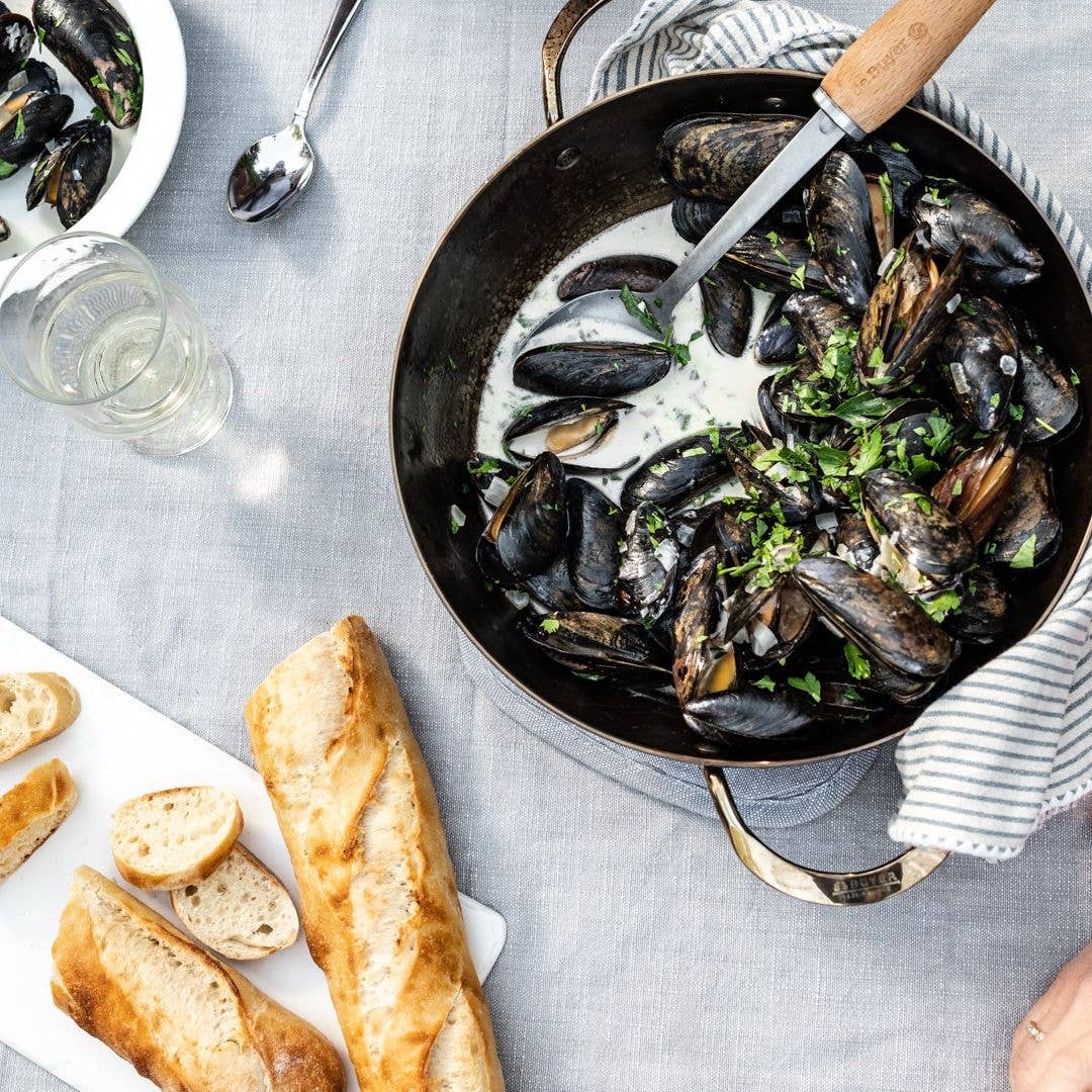 Mussels in a creamy sauce with bread on a gray tablecloth