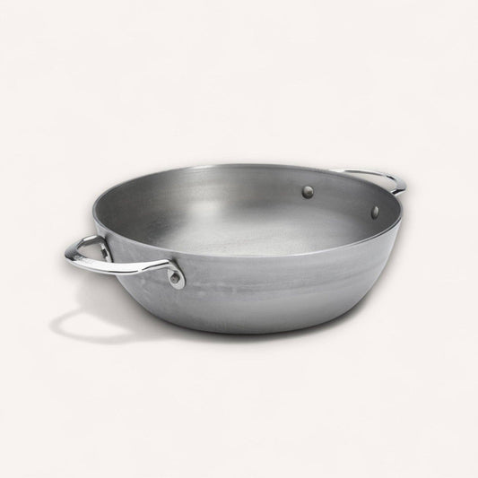 A carbon steel deep pan with two side handles, photographed on a clean off-white background.