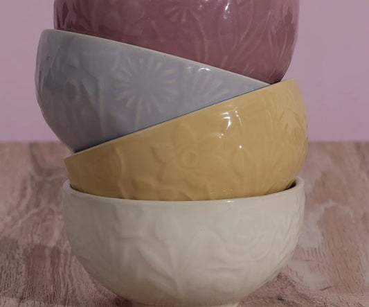 Stack of ceramic bowls in gray, yellow, and white with floral patterns on a wooden surface.