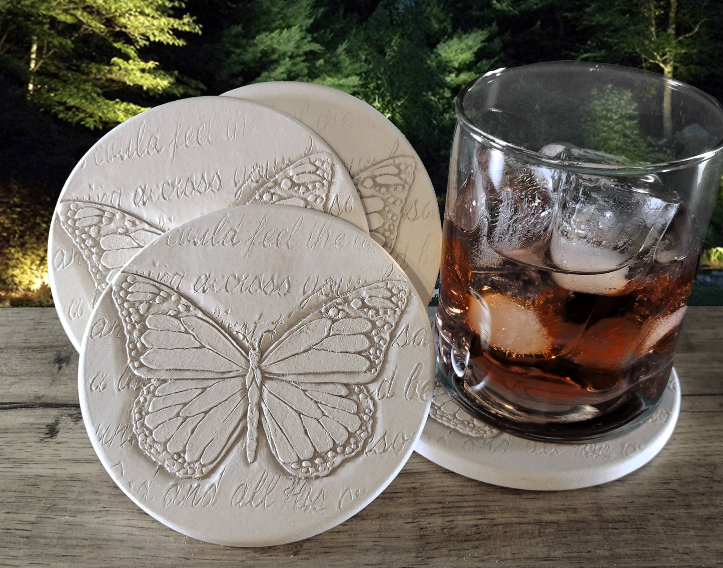 Butterfly-patterned coasters with a glass of iced tea on a wooden surface outdoors.
