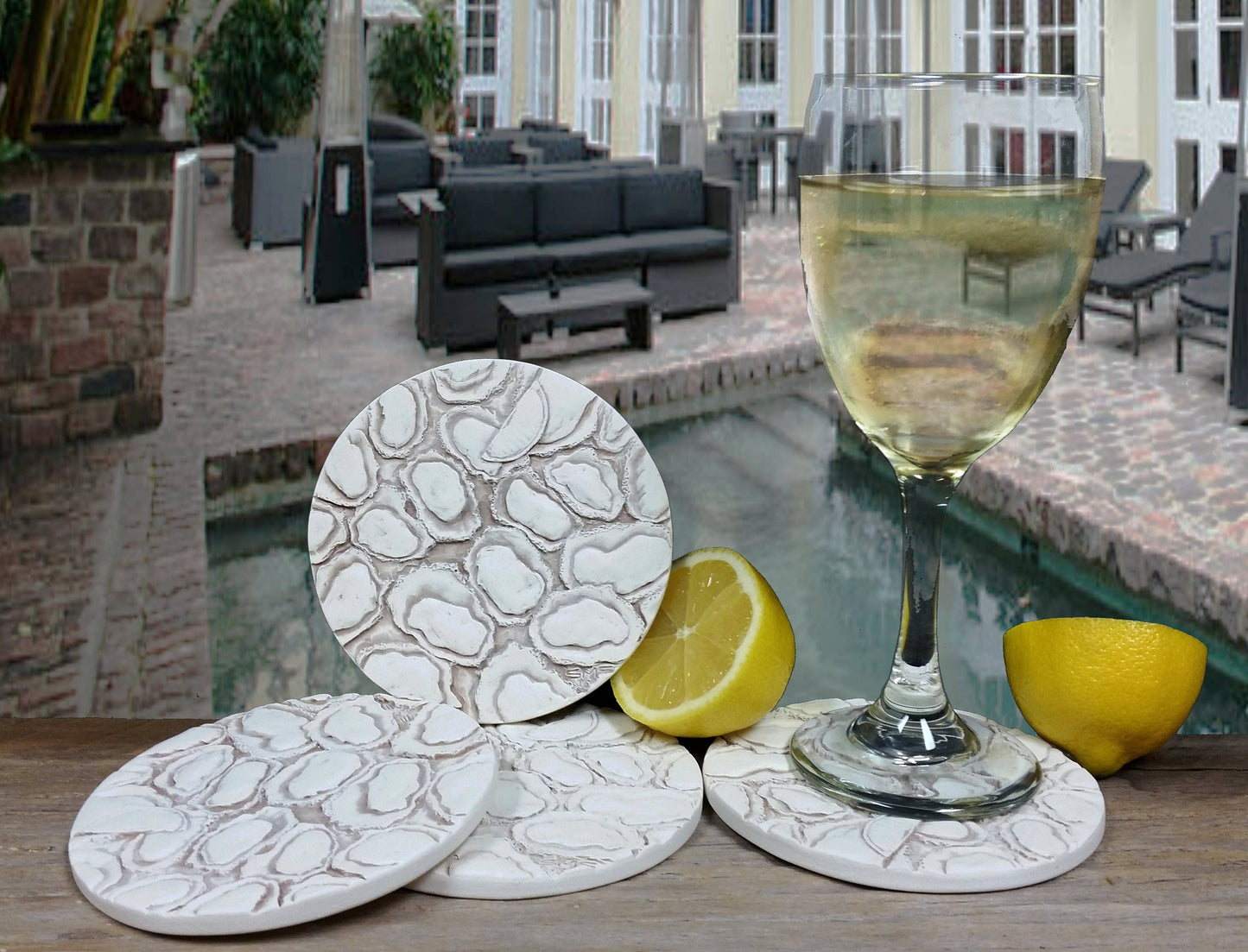 Set of stone coasters with a glass of wine and lemons on a table by a poolside.