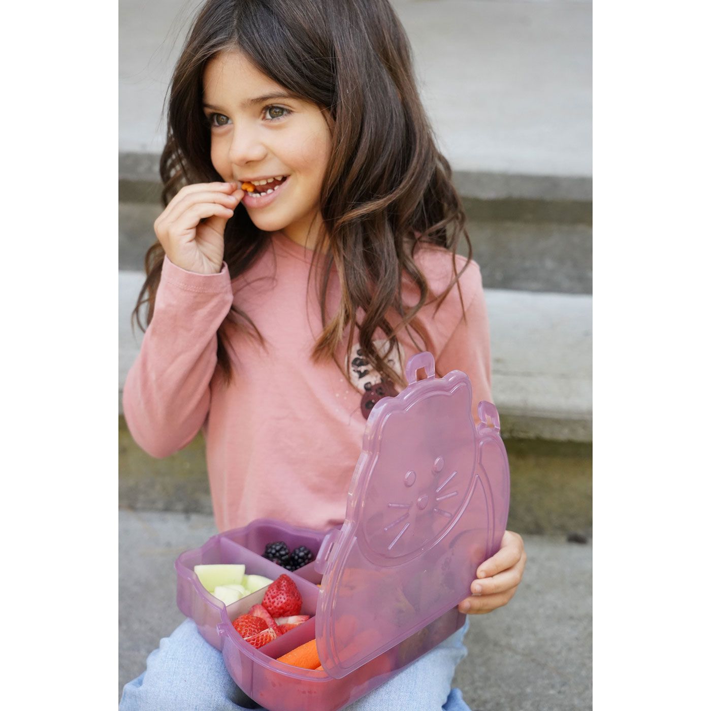 Child holding a pink lunchbox with snacks outdoors