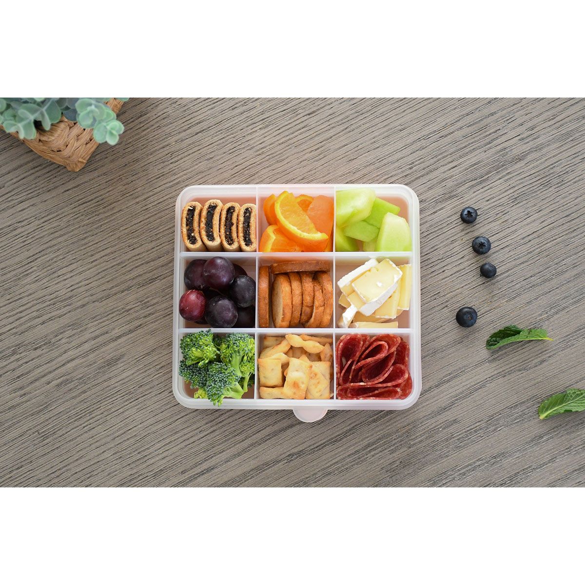 Divided lunch container with various food items on a wooden surface