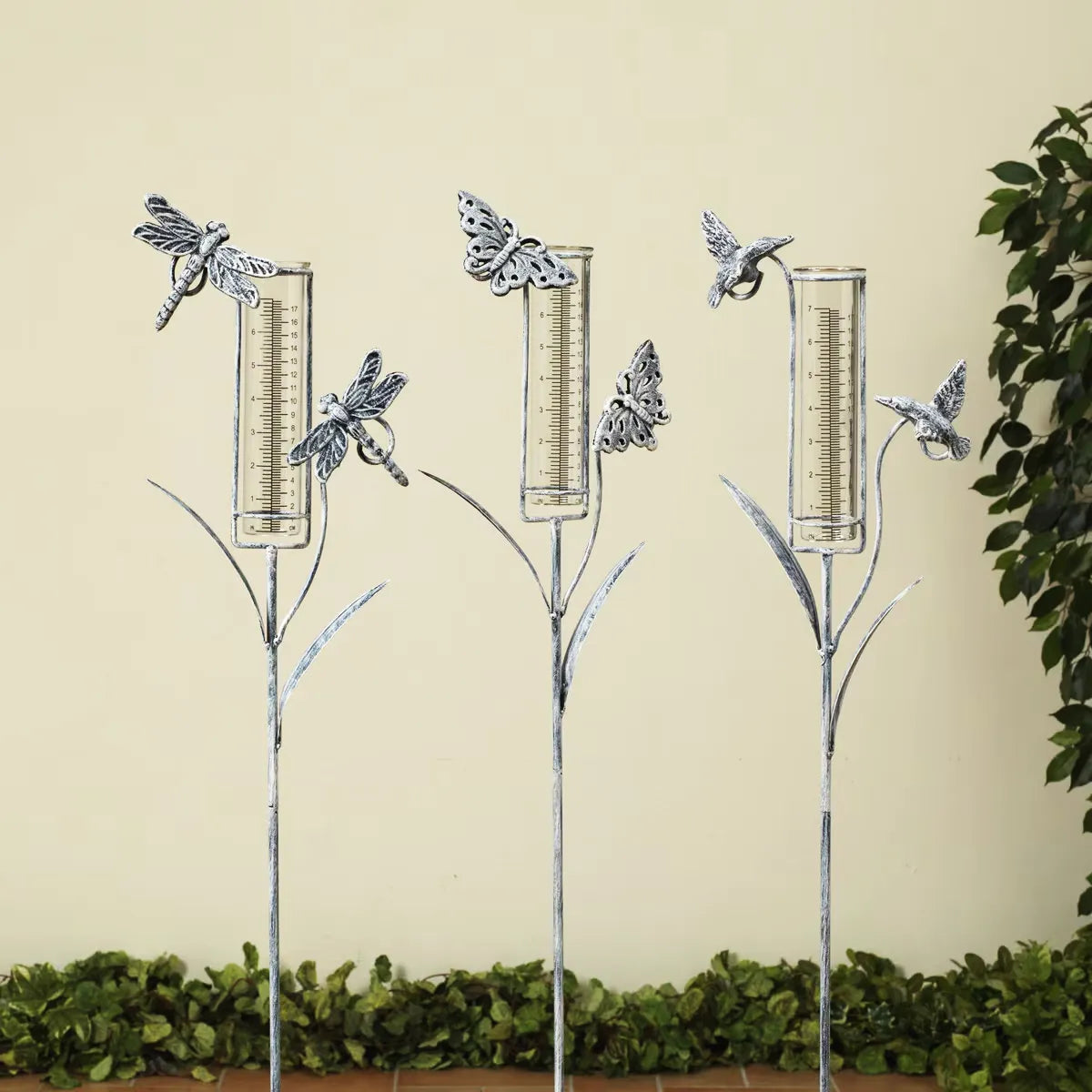 Decorative garden stakes with rain gauges shaped like butterflies, dragonflies, and hummingbirds against a beige background.