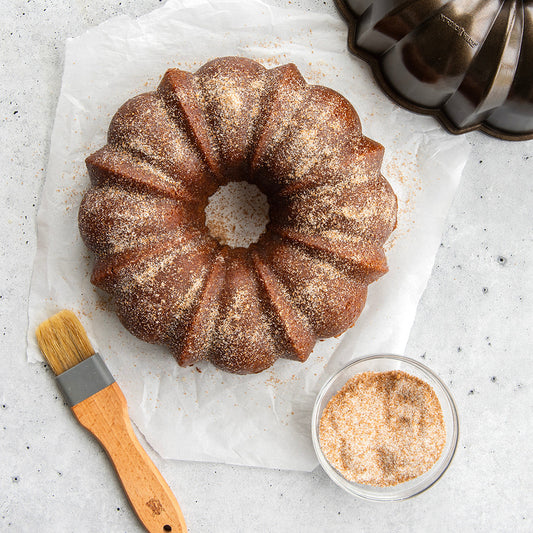 Bundt cake with sugar glaze, brush, and bowl on a light surface