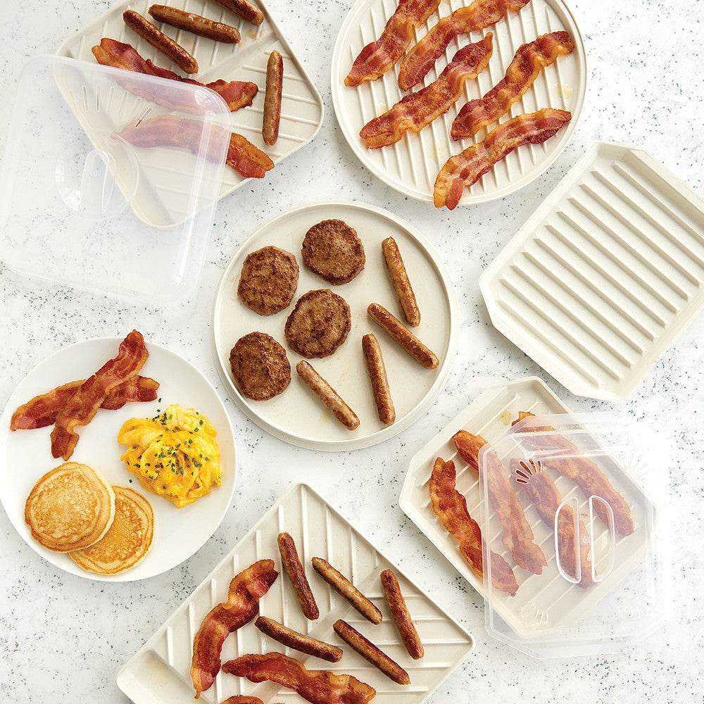 Assorted breakfast items including bacon, sausages, pancakes, and eggs on a light surface.