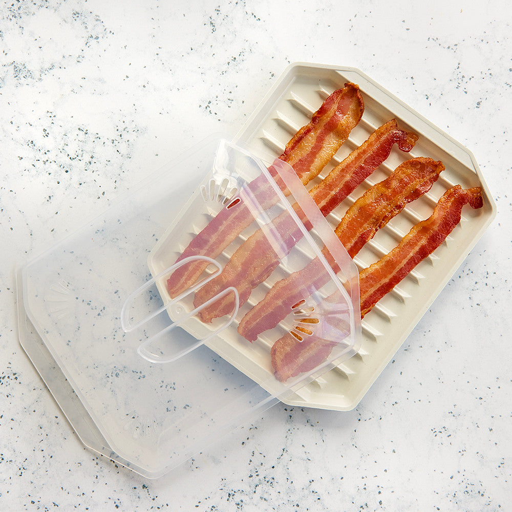 Bacon slices on a white microwave
 pan with a transparent lid on a speckled countertop.