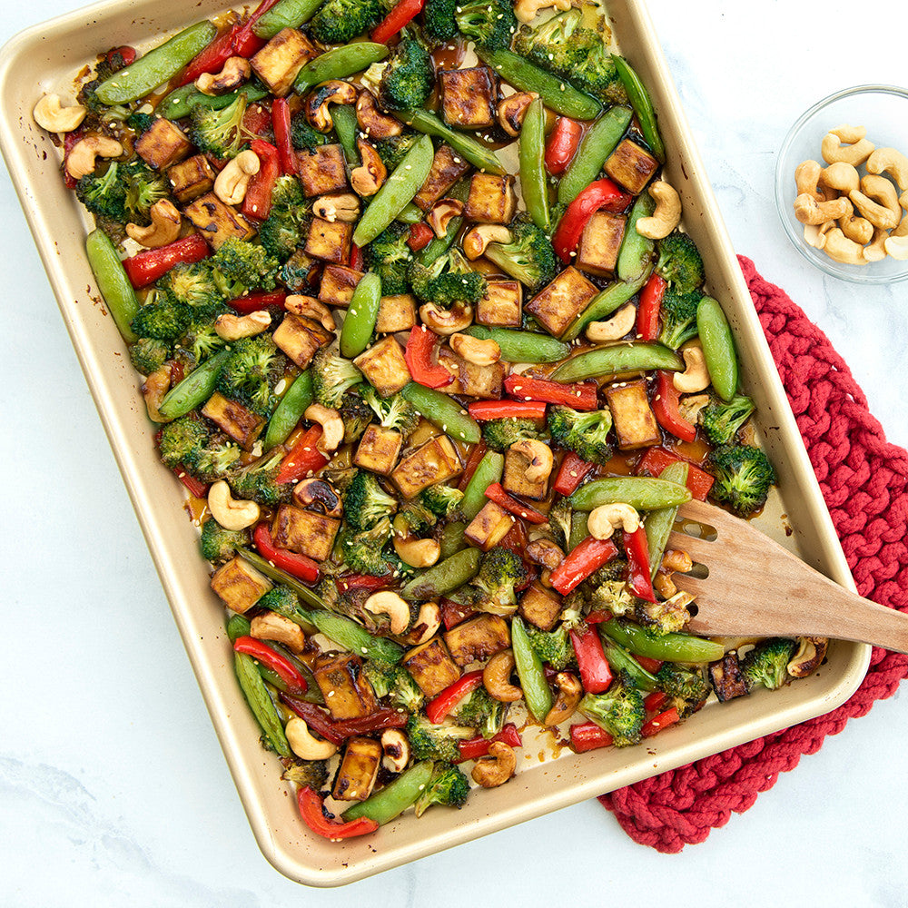 Roasted vegetable dish with cashews in a baking tray on a white surface.