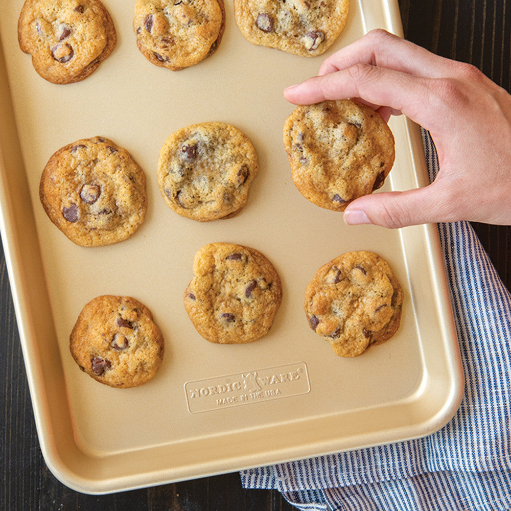 Hand picking a chocolate chip cookie from a baking tray with 'Gold Medal' branding.