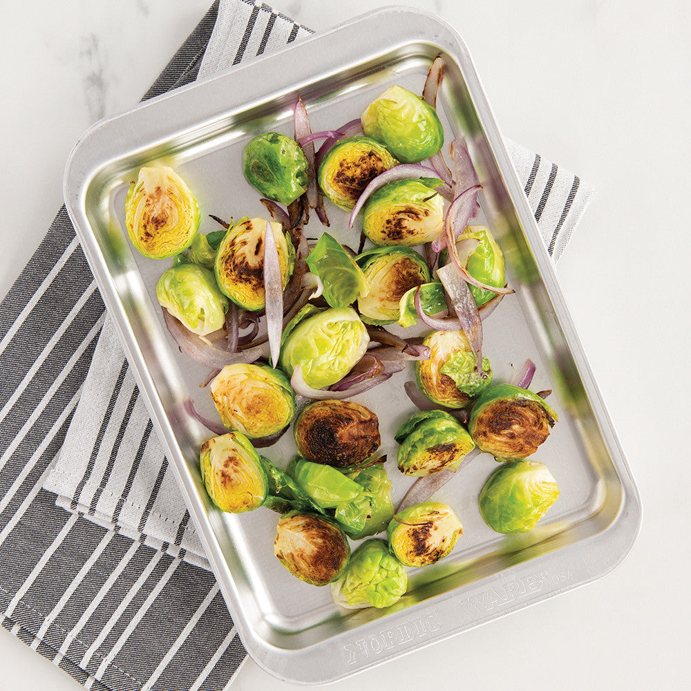 Roasted Brussels sprouts with onions on a metal baking tray.