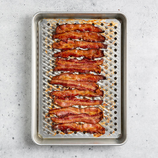 Bacon strips on a perforated baking sheet on a gray surface
