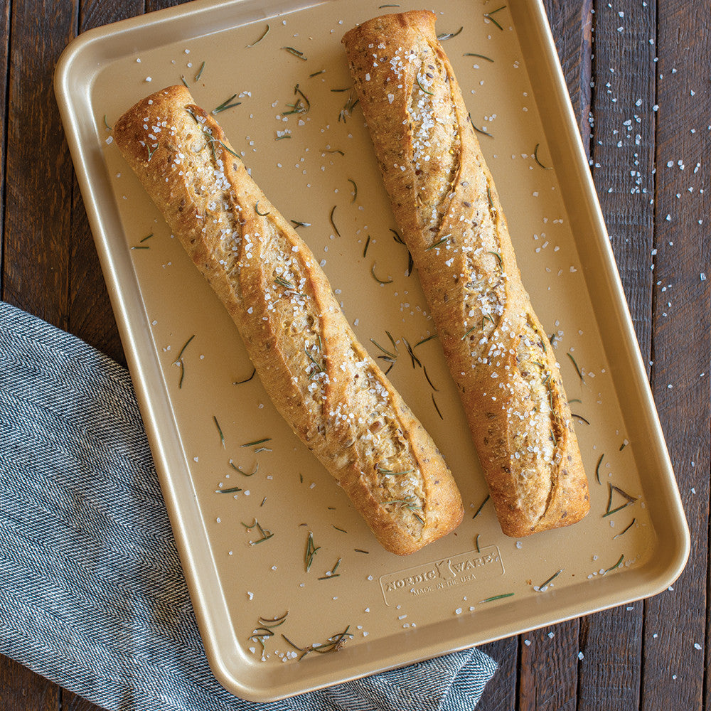 Two bread sticks on a baking tray with herbs and salt, placed on a wooden surface.