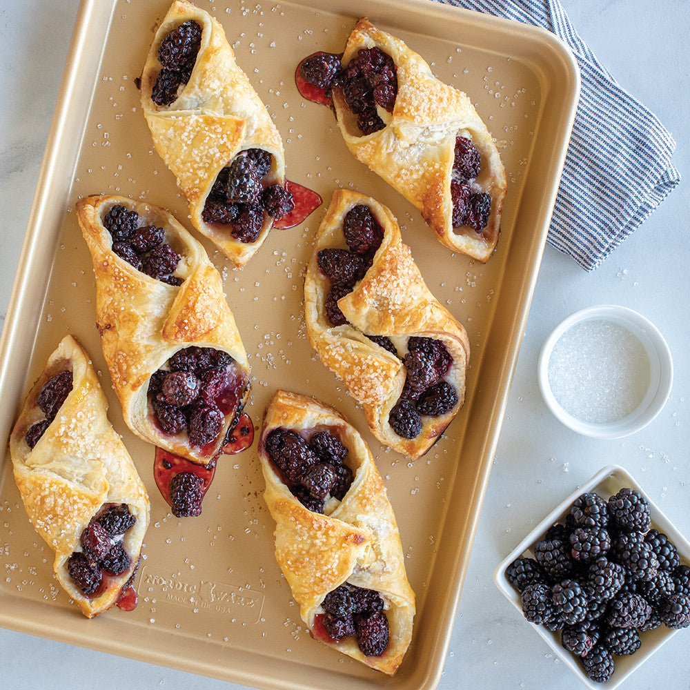 Pastry triangles with berry filling on a baking tray, next to a bowl of berries.