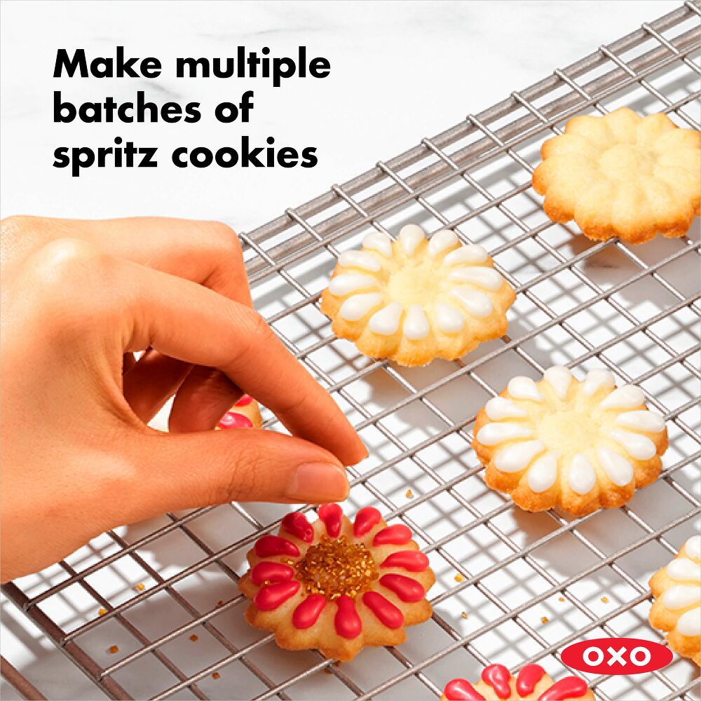 Hand arranging decorated spritz cookies on a cooling rack with OXO branding.