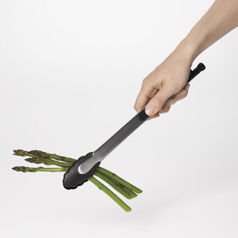 Hand holding an OXO Stainless Steel Tongl with asparagus on a white background