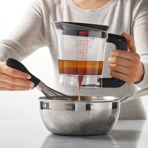 Person pouring liquid from a fat separator into a bowl with a whisk.