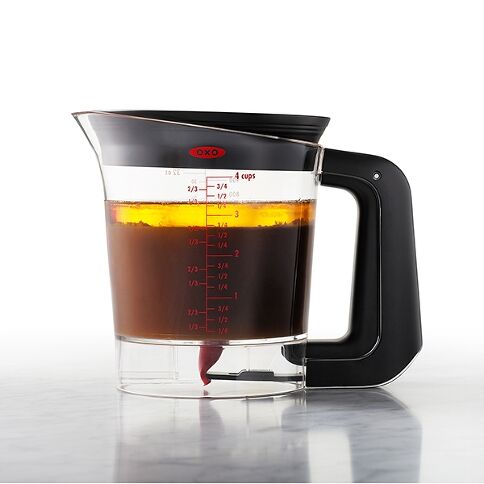 Black and clear glass fat strainer
 with red measurement markings on a white background