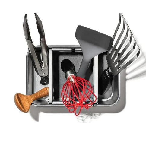 Set of kitchen utensils including tongs, spatula, whisk, and ladle in a metallic holder on a white background.