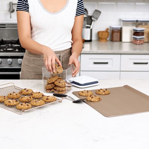 Person in a kitchen with cookies on a baking sheet and a clear container.
