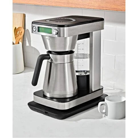 Coffee maker on a kitchen counter with a digital display and a white mug nearby.