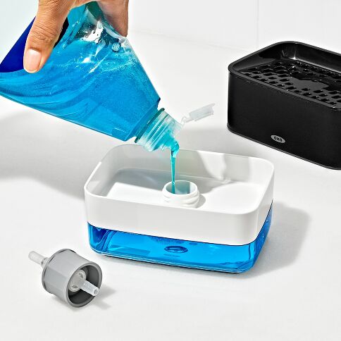 Person pouring blue liquid into a white and blue soap dispenser on a white background
