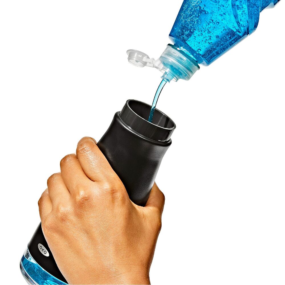 Hand pouring blue liquid from a bottle into a black OXO soap disoenser on a white background