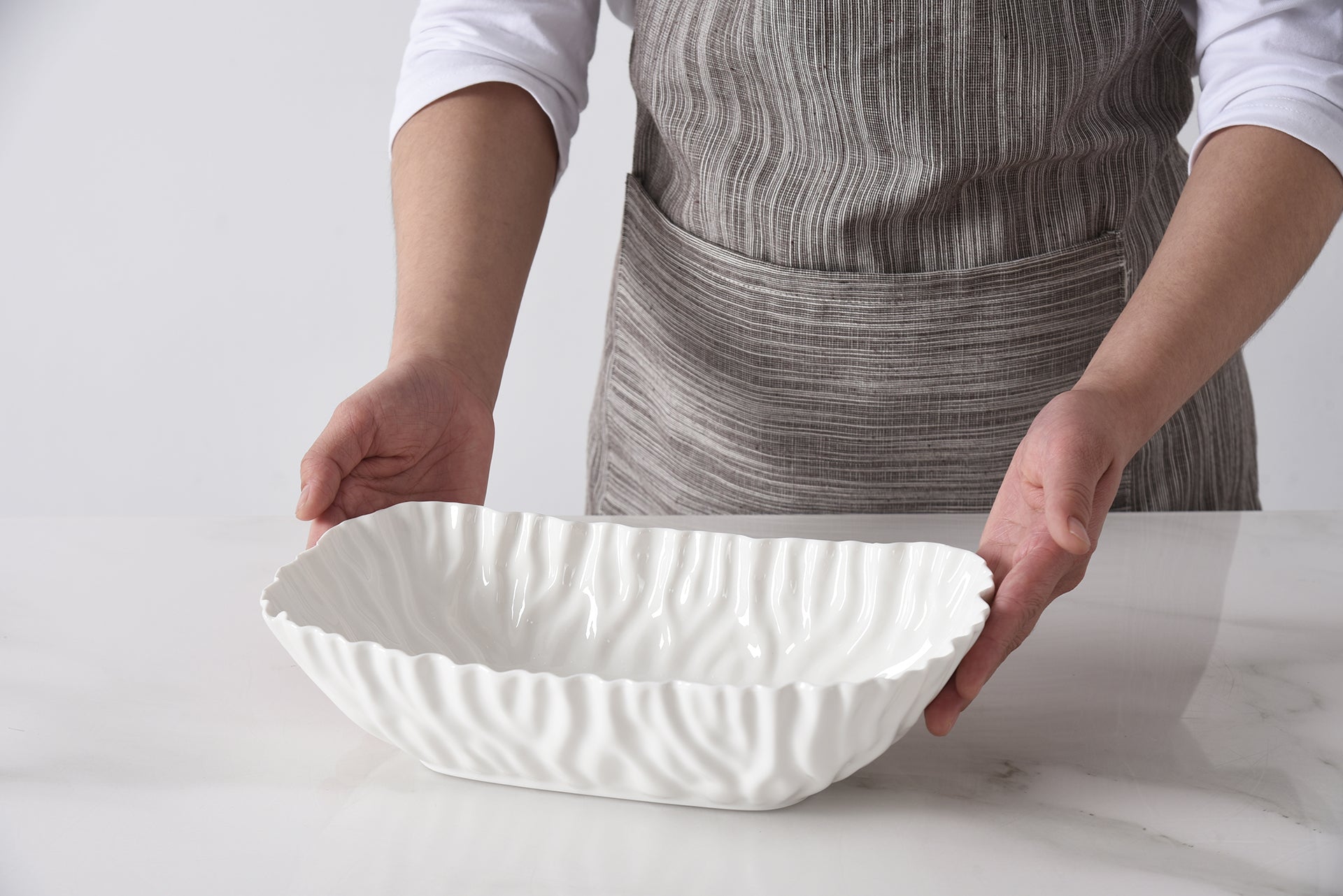 Person holding a white ceramic dish on a marble surface