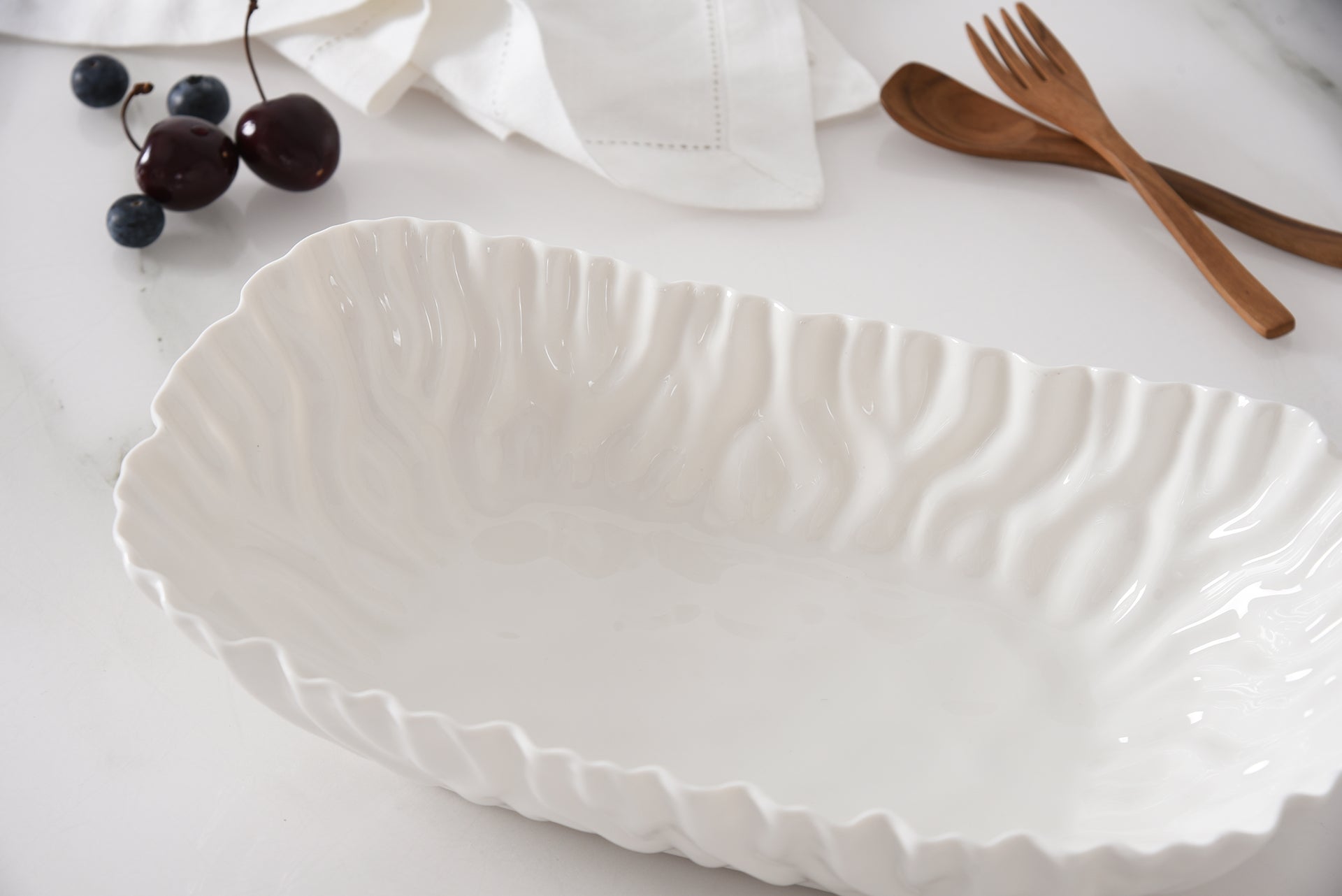 White ceramic serving dish on a white surface with wooden utensils and grapes.