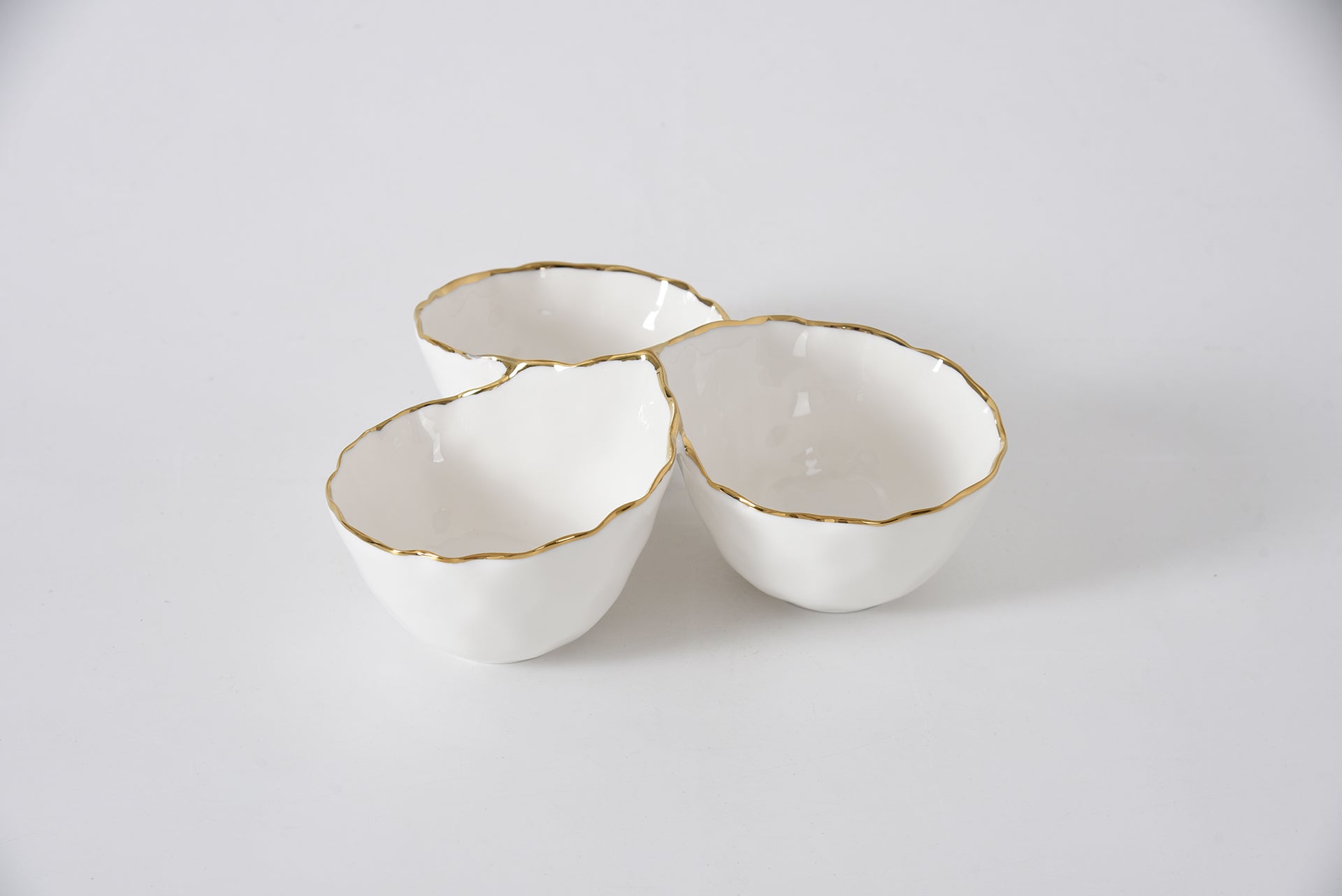 Three white ceramic bowls with gold rims on a light gray background