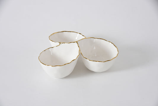 Three white ceramic bowls with gold rims on a light gray background