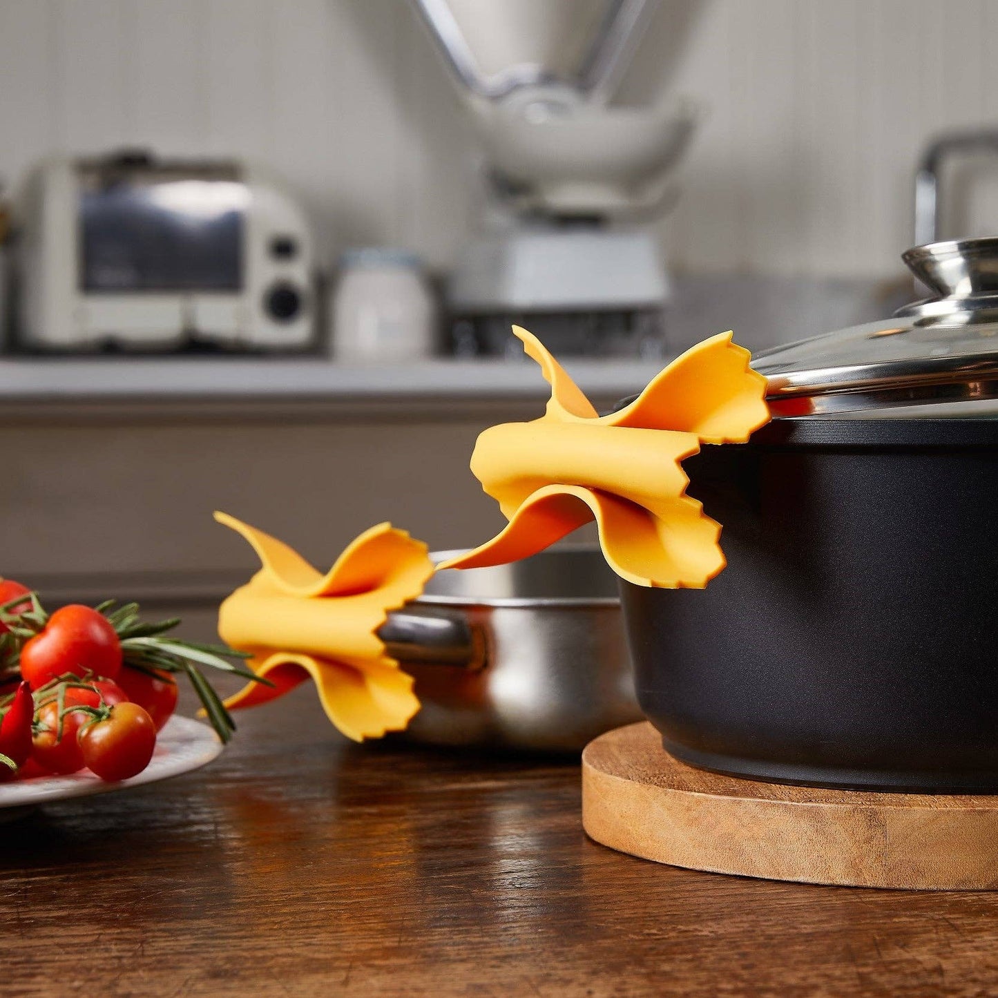Black pot on a wooden trivet with decorative yellow flowers and red peppers on a kitchen counter.
