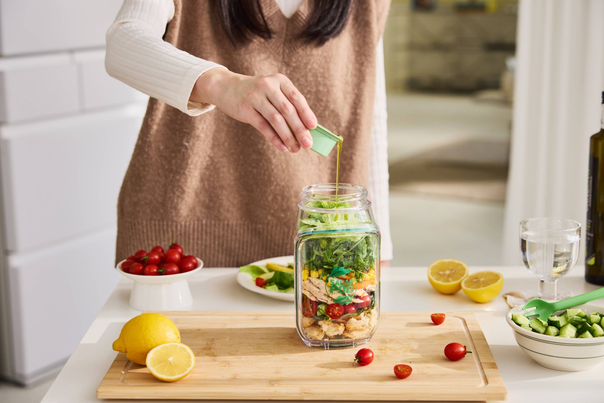 Person preparing a salad in a jar with ingredients on a kitchen counter.