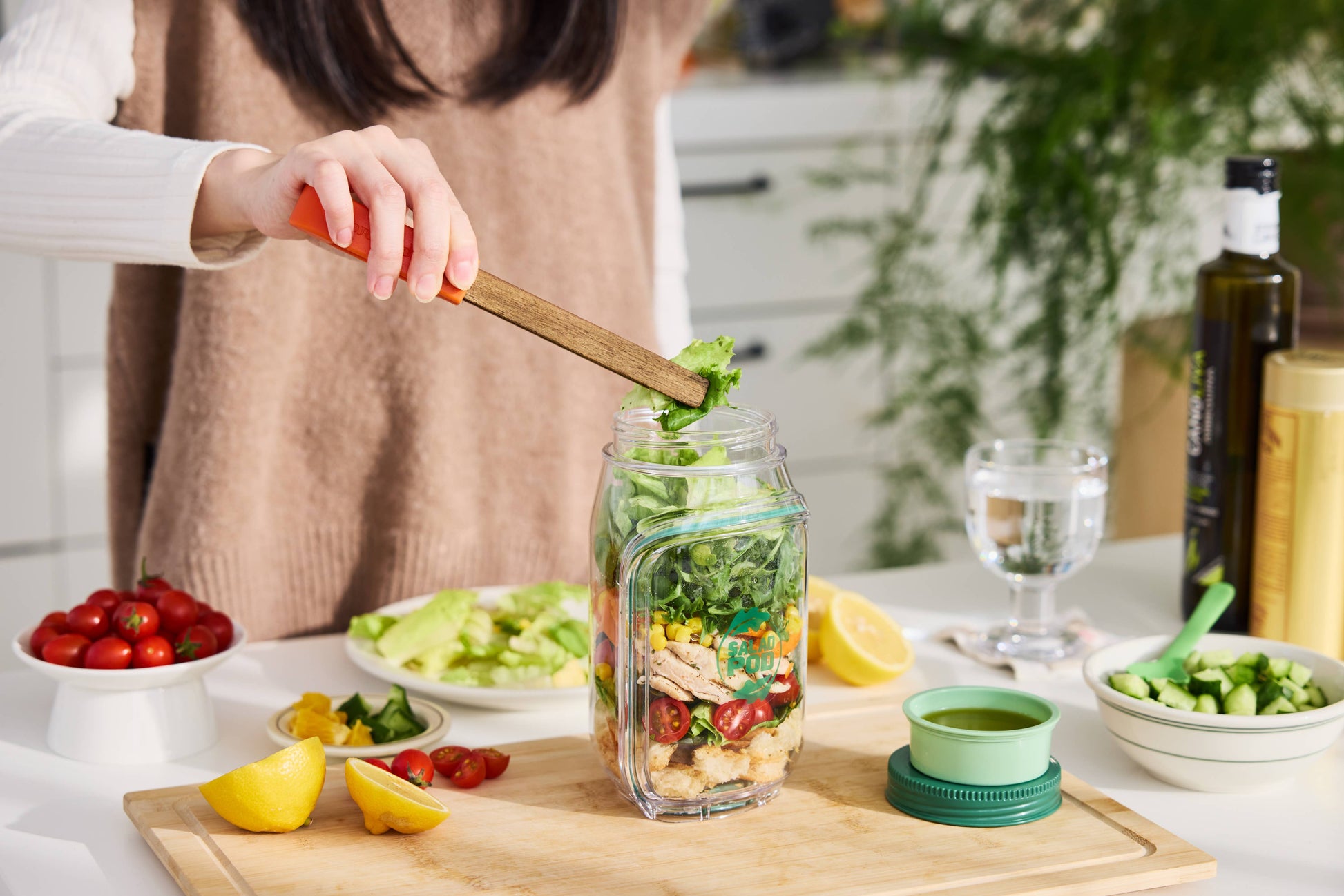 Person preparing a salad in a jar with ingredients on a kitchen counter.