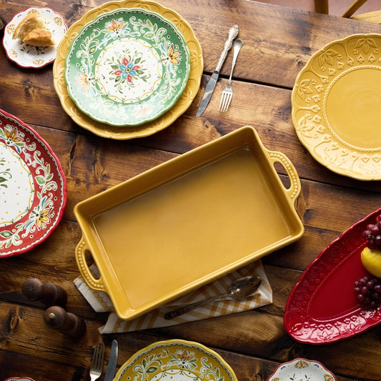 Collection of colorful ceramic plates and a yellow baking dish on a wooden table.