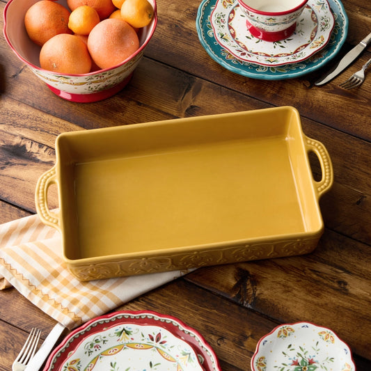 Yellow ceramic baking dish on a wooden table with decorative plates and oranges.