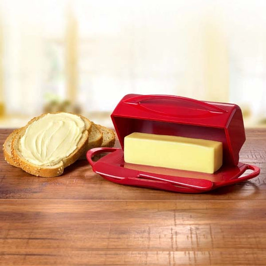 Red butter spreader with a stick of butter on a wooden surface next to a slice of bread.
