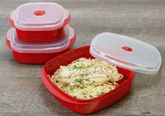 Red food storage containers with a lid, one containing pasta and chicken on a wooden surface.
