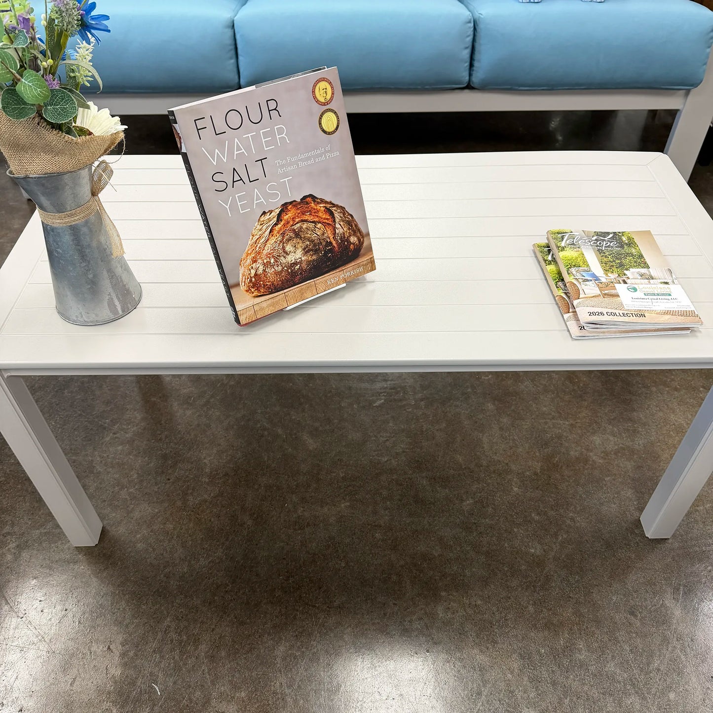 Table with a cookbook titled 'Flour Water Salt Yeast' and a vase of flowers in a room.