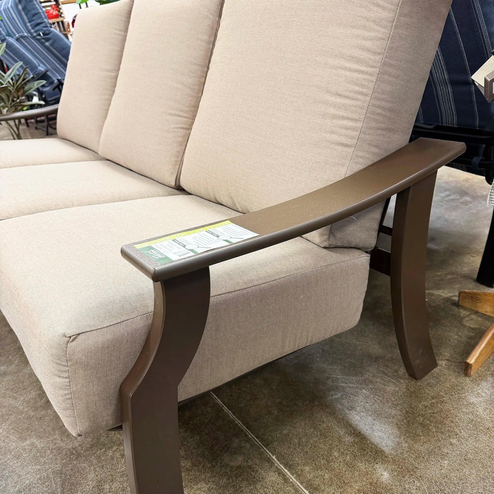 Beige outdoor sofa with a brown armrest table in a store setting