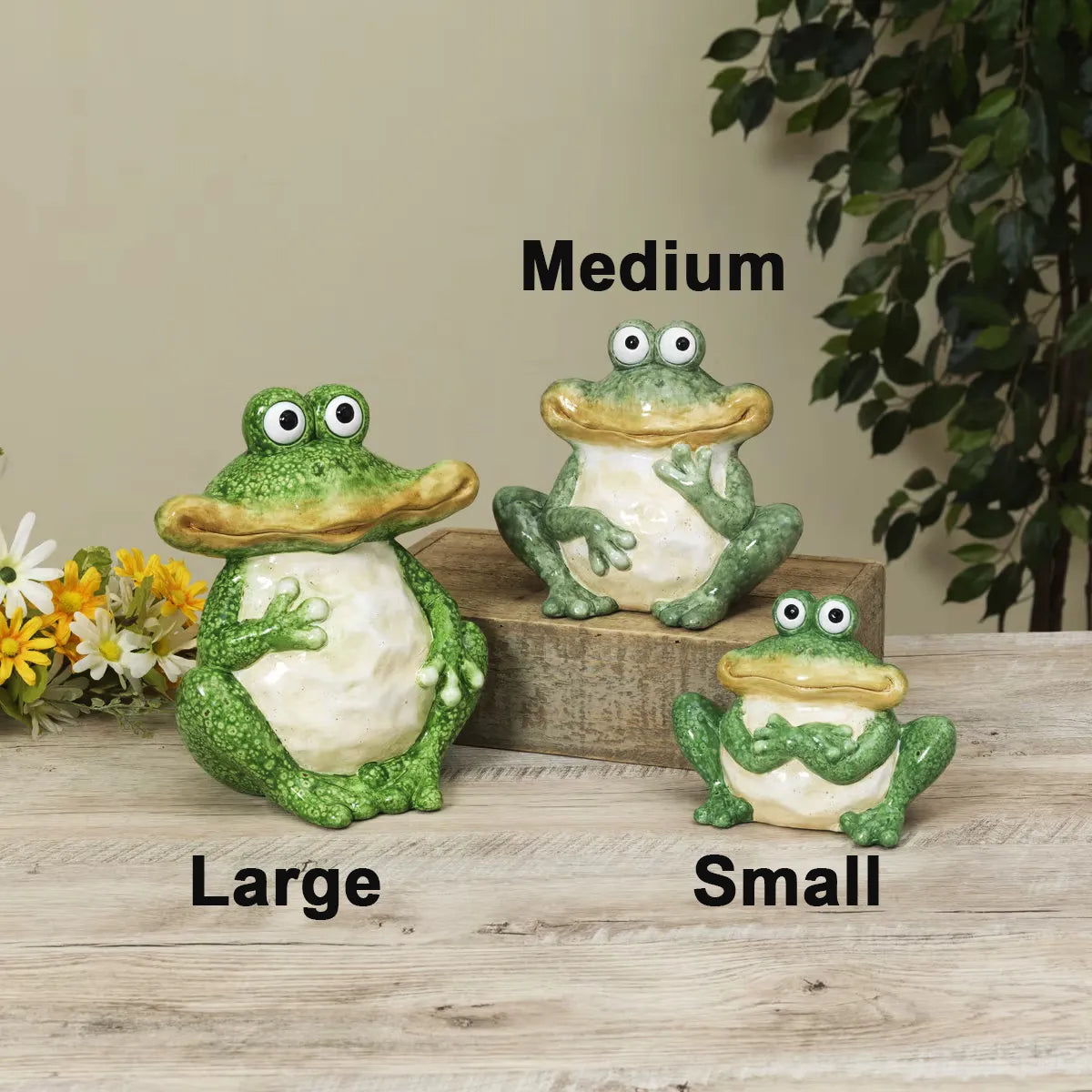 Three frog statues labeled 'Large', 'Medium', and 'Small' on a wooden surface with flowers and leaves in the background.