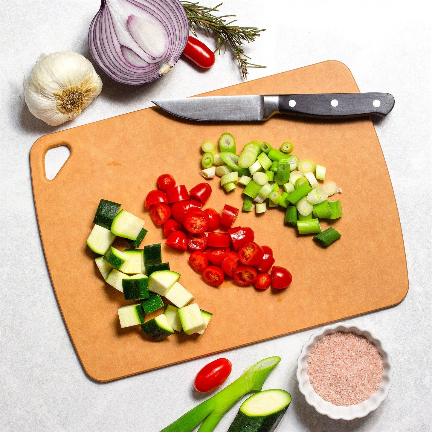 Chopped vegetables on a cutting board with a knife, garlic, and salt.
