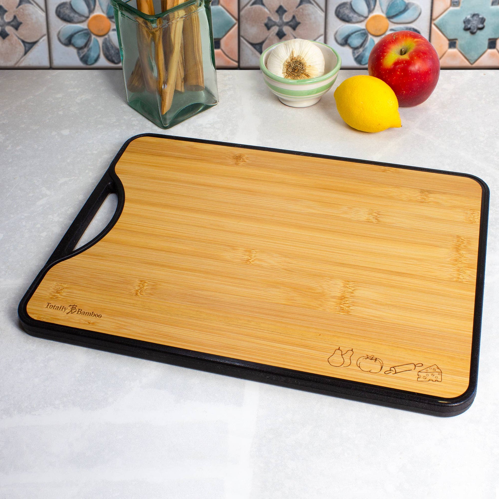 Wooden cutting board with black handle on a kitchen counter with fruits and vegetables.