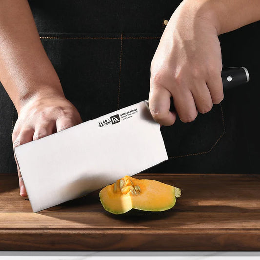Person using a chopping knife to cut a piece of fruit on a wooden cutting board.