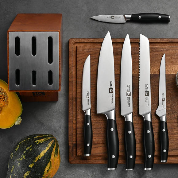 Set of knives with black handles on a wooden cutting board, next to a knife block and pumpkins.