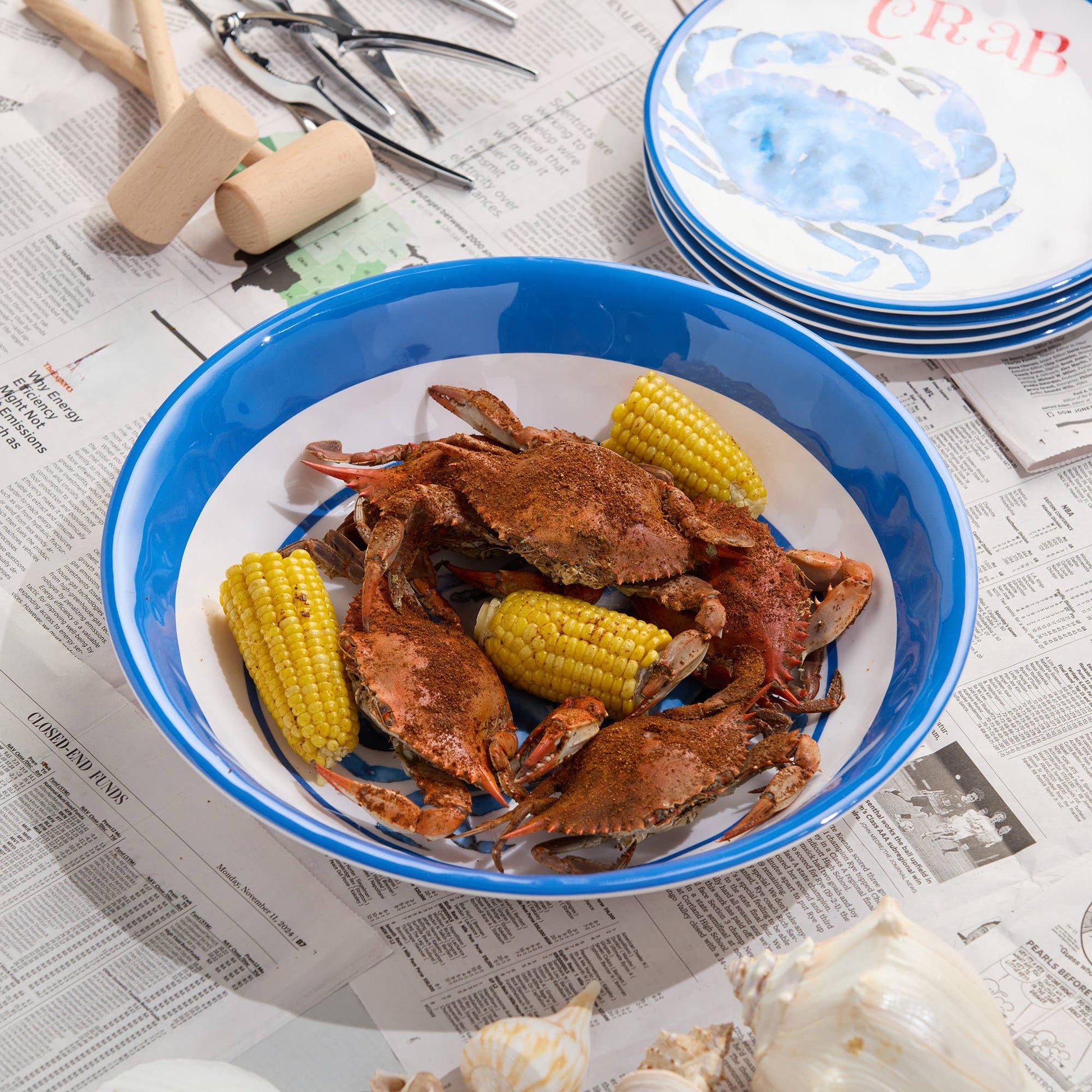 Platter of crabs and corn on a blue rimmed plate with a newspaper background