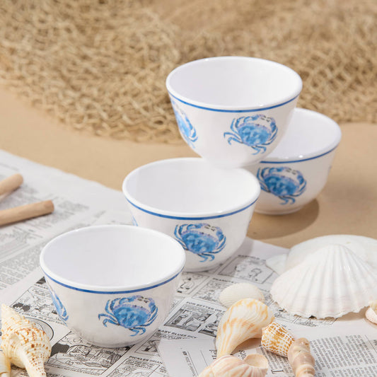 Set of white bowls with blue crab design on a newspaper with shells and beach sand background