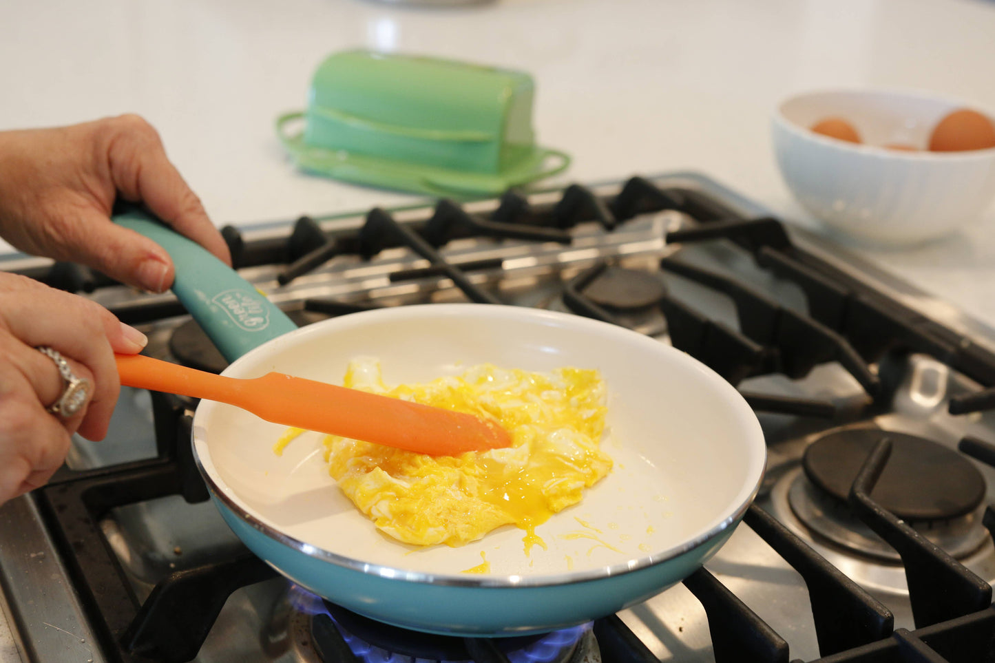 Person cooking eggs in a pan on a stove with a Butterie orange silicone spatula