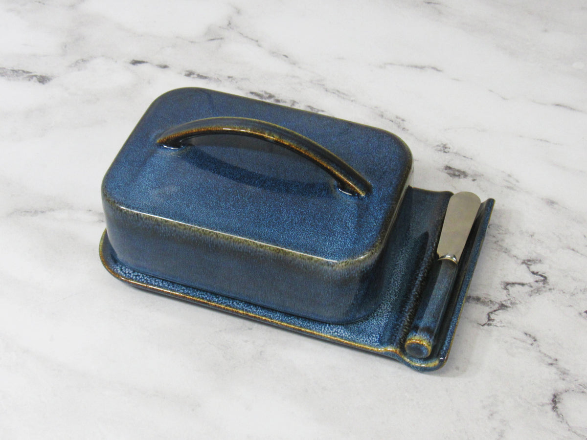 Blue ceramic butter dish with knife on a marble surface